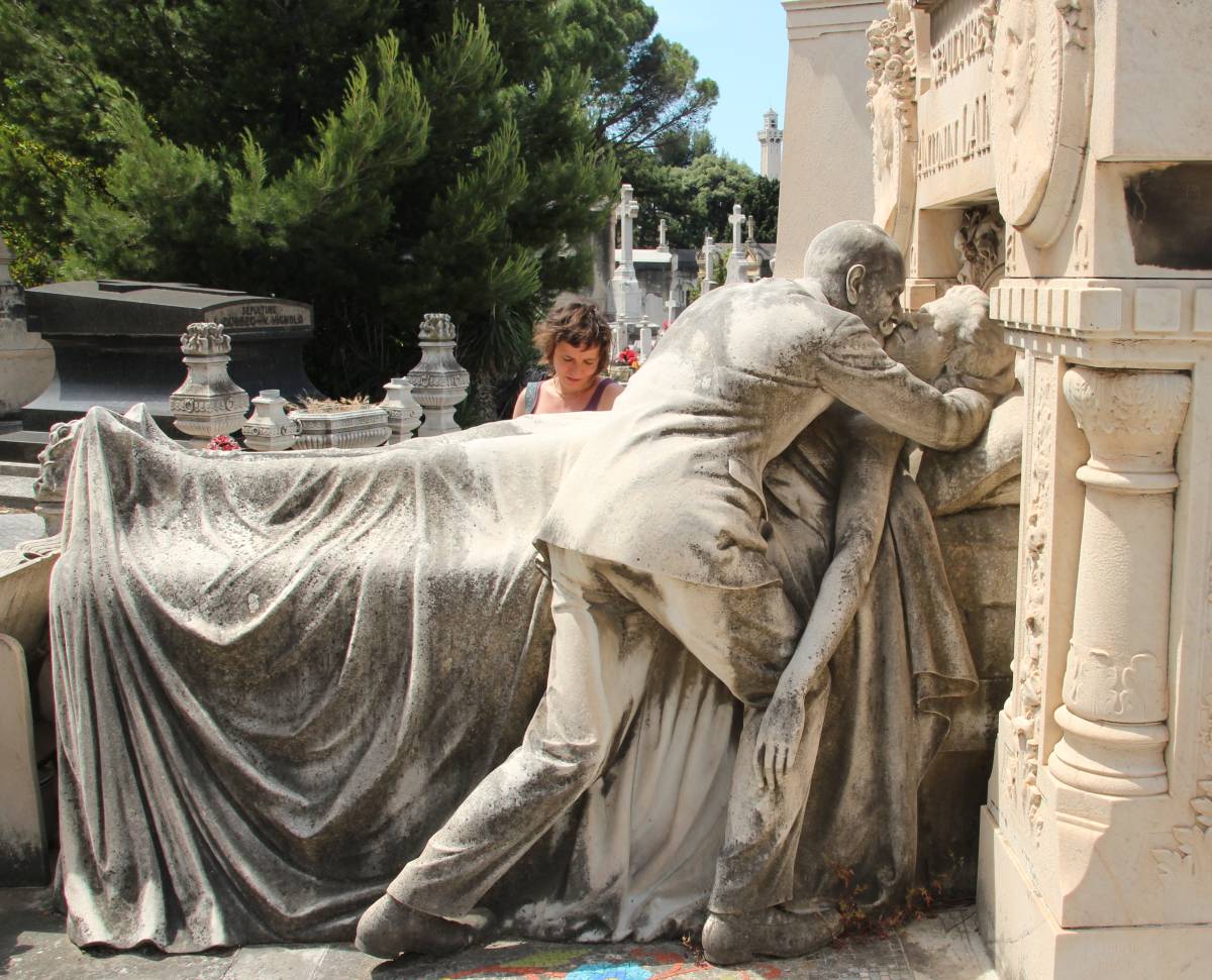 Ein Grabstein vom Friedhof in Marseille zeigt eine lebensgroße Skulptur von einem Mann, der sich zu seiner Frau niederbeugt, die sterbend im Bett liegt.